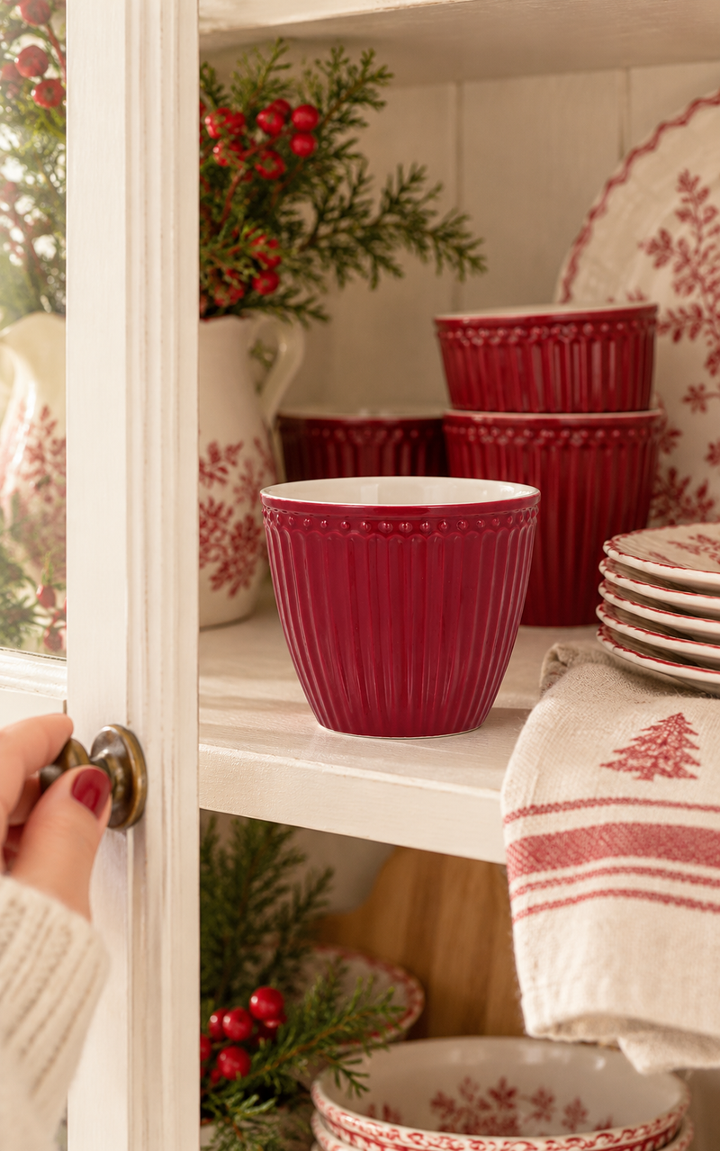 Tazza latte GreenGate Alice Claret Red in ceramica bordeaux con scanalature verticali, esposta in una vetrinetta natalizia bianca stile cottage.