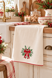 Strofinaccio natalizio in cotone crema con fiocco rosso e agrifoglio ricamato, ambientato in cucina stile cottage inglese.